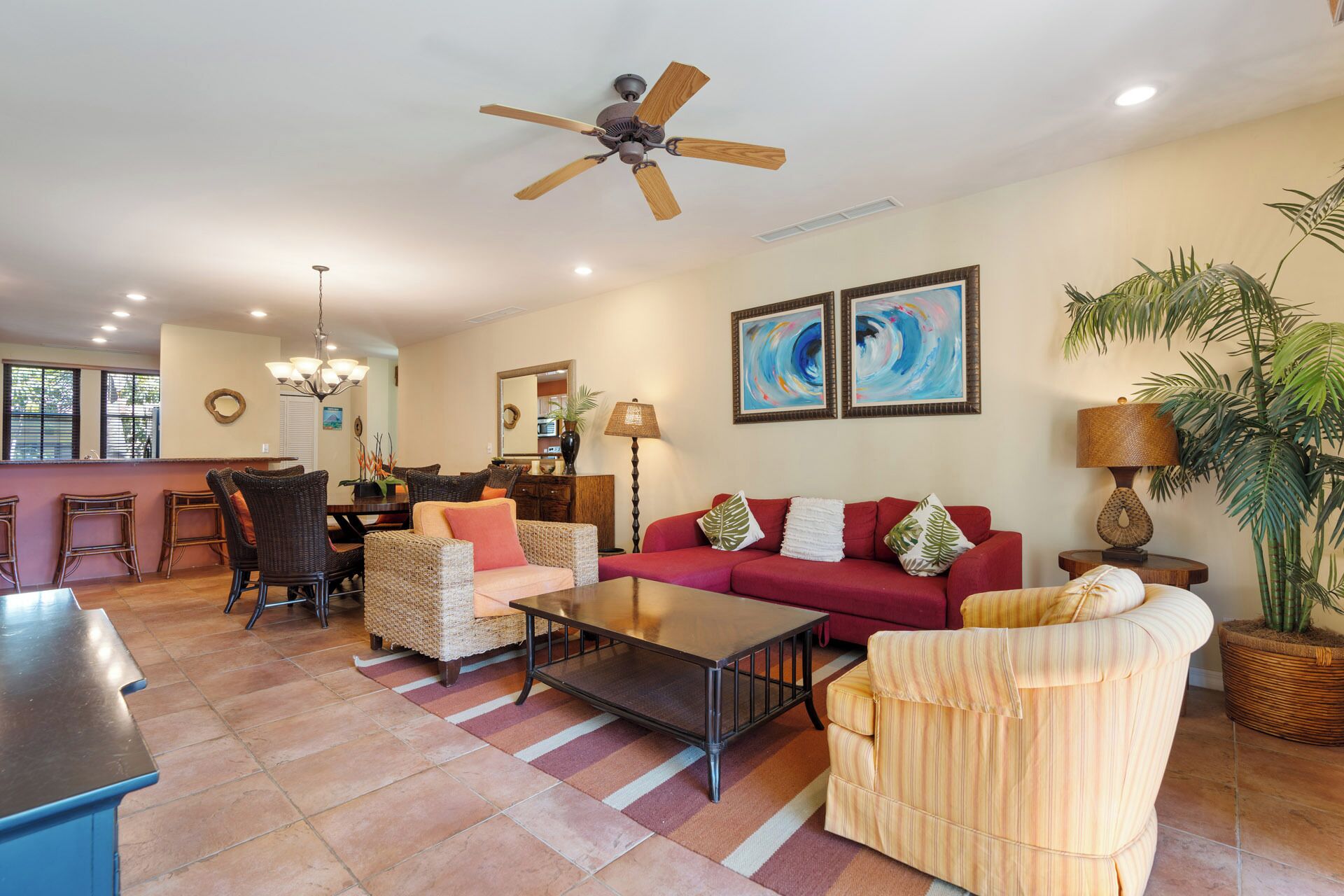 A spacious living area with a red sofa, wicker chairs, a coffee table, and a ceiling fan.
