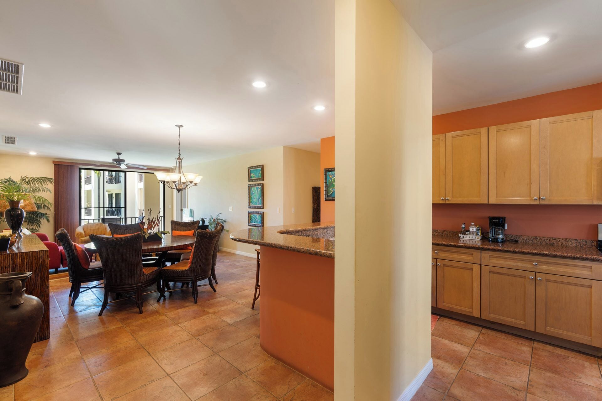 A modern kitchen with wooden cabinets, a granite countertop, and a dining area with wicker chairs and a central island.