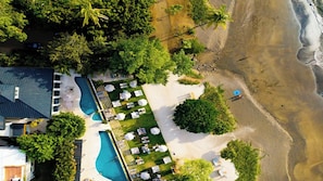 An aerial view of a resort with a swimming pool, beach, and lush greenery. - Modern One-Bedroom Condo with Pool Views, Beach Club Access & Resort Amenities (Sardinal)
