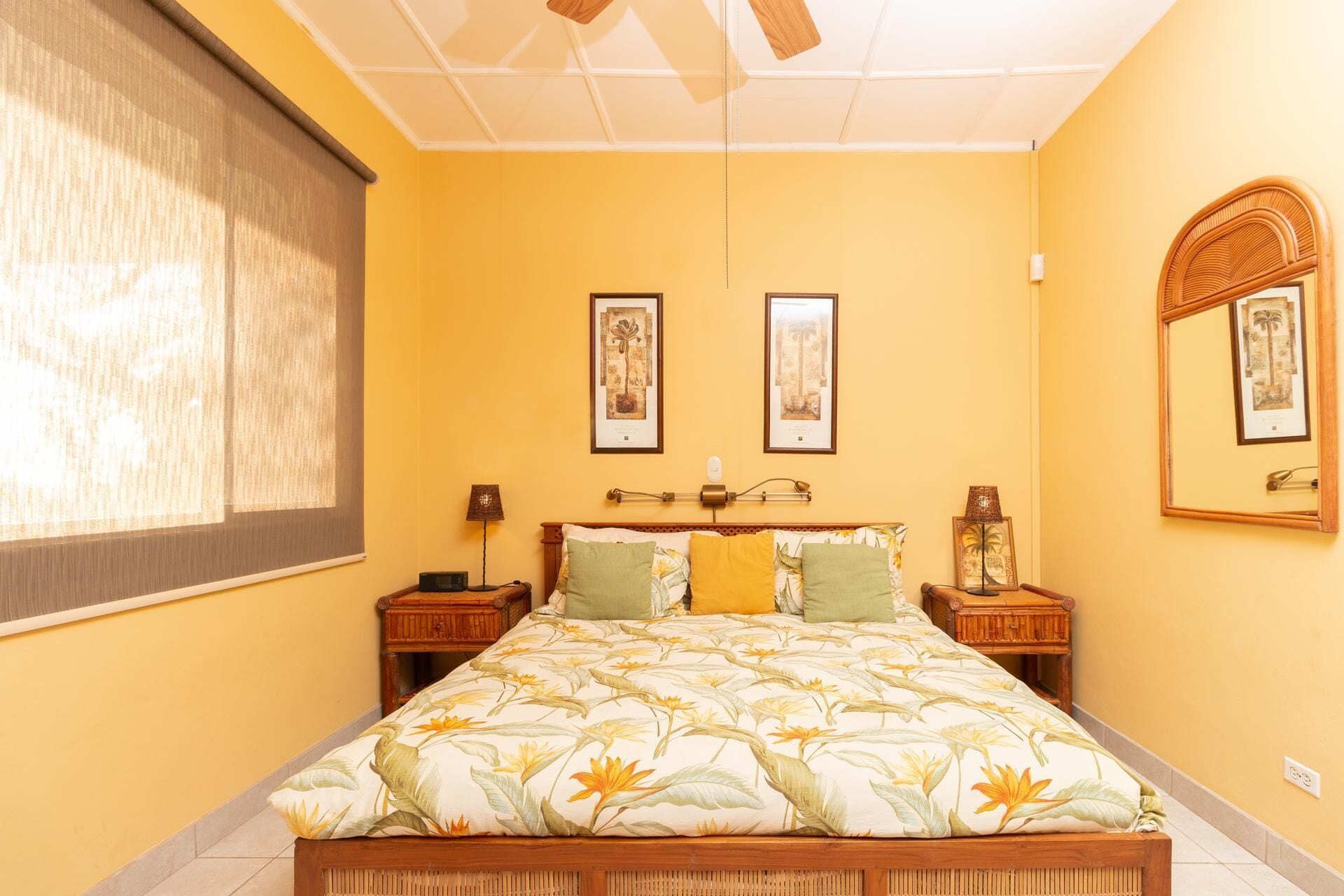 A bedroom with a bed, two bedside tables, a nightstand, a ceiling fan, and two framed pictures on the wall.