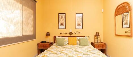 A bedroom with a bed, two bedside tables, a nightstand, a ceiling fan, and two framed pictures on the wall.