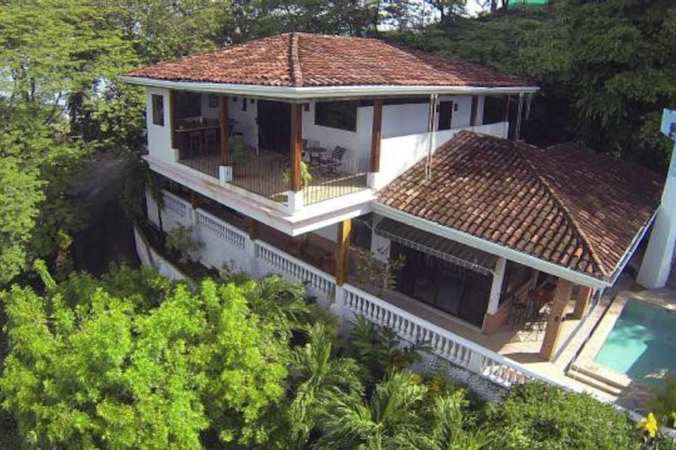 A two-story house with a tiled roof, a balcony, and a swimming pool.