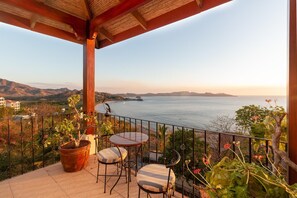 A terrace with a table and chairs, overlooking a coastal view with mountains in the distance. - Luxury Flamingo villa with outdoor bar - pool and magnificent views (Cabo Velas)