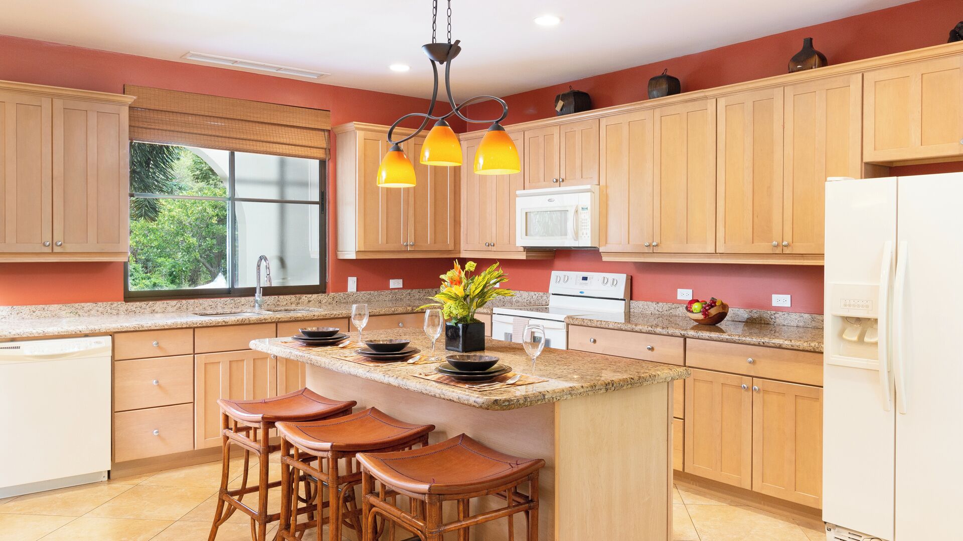 A kitchen with wooden cabinets, a granite countertop, a central island with stools, a microwave, and a refrigerator.