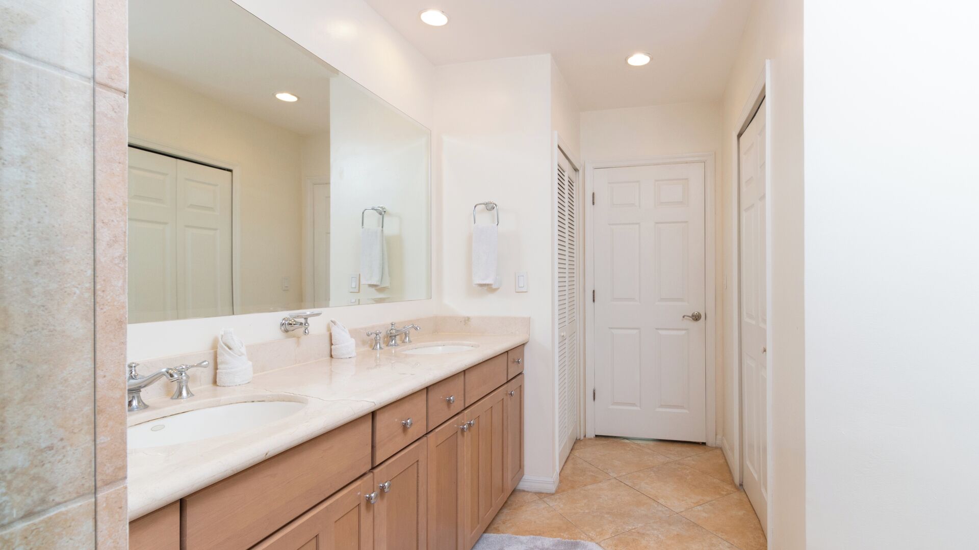 Une salle de bain avec deux lavabos, un grand miroir et une porte donnant sur une autre pièce.