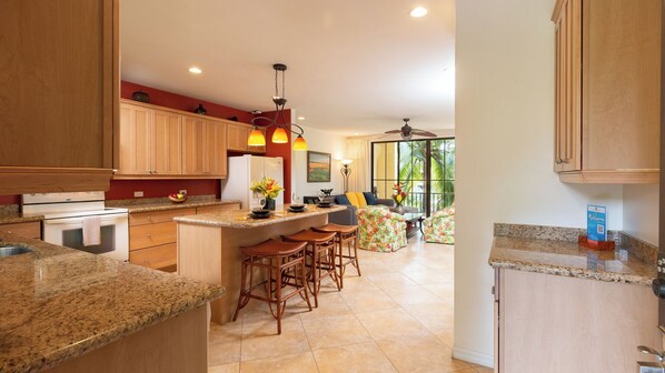 A kitchen with granite countertops, wooden cabinets, a central island with stools, and a dining area with a view.