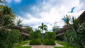 A courtyard with a stone pathway, palm trees, and a building with a flat roof. - Nicely decorated 3rd-floor beauty with pool-view balcony in Coco (Sardinal)