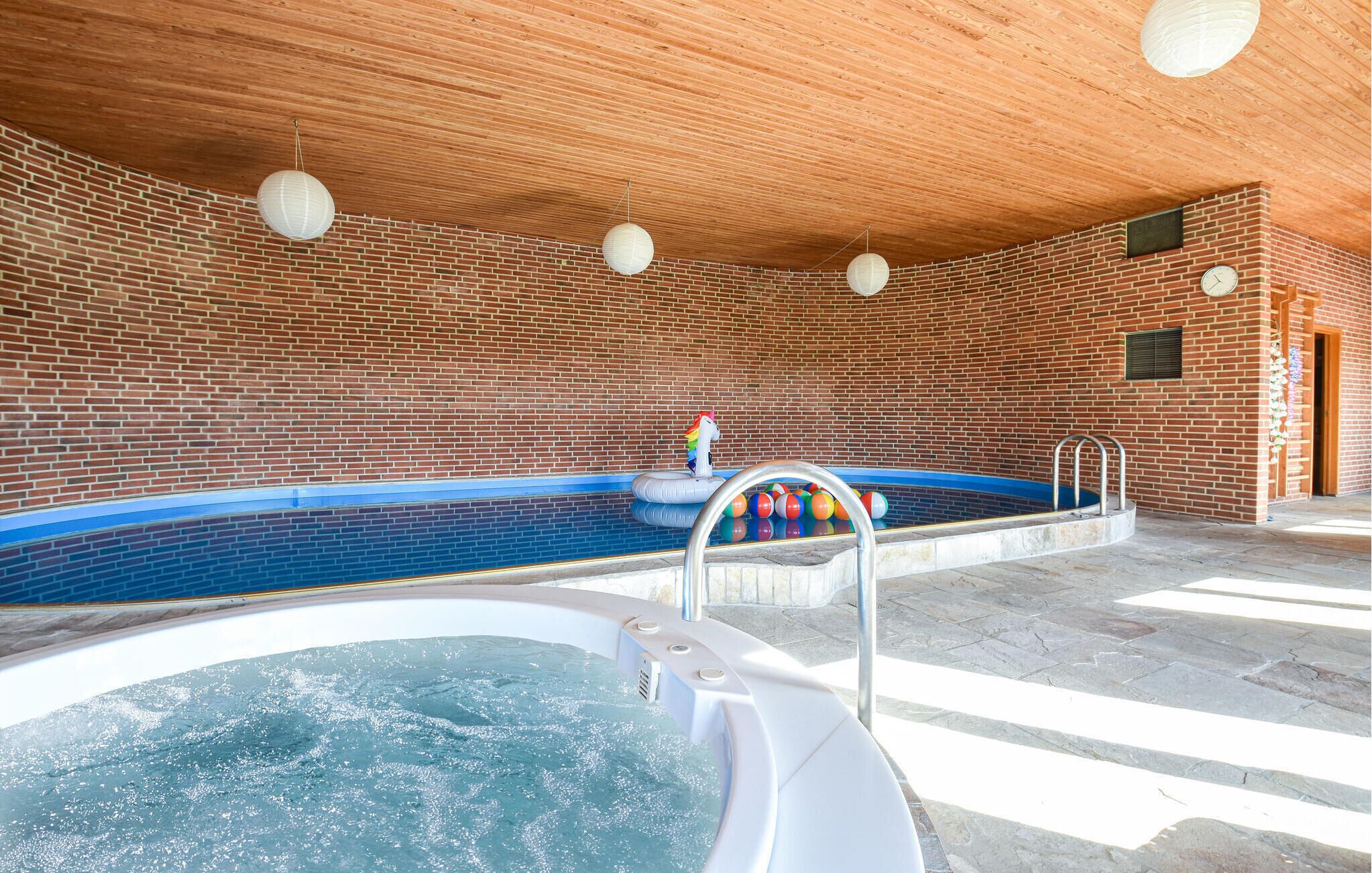 A swimming pool with a hot tub, surrounded by a brick wall and wooden ceiling.