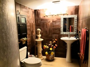 Bathroom features a pedestal sink, shower area, and toilet, with decorative touches and storage.