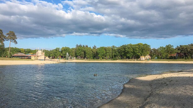 Une plage à l’eau claire, un rivage sablonneux et une rangée de bâtiments en arrière-plan.
