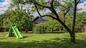 Une zone herbeuse avec un toboggan vert et un bâtiment en bois en arrière-plan.