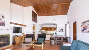 A spacious living area with a fireplace, a television, and a dining area with a kitchen in the background. - Villa Jacaranda V3 by Interhome (Albufeira)