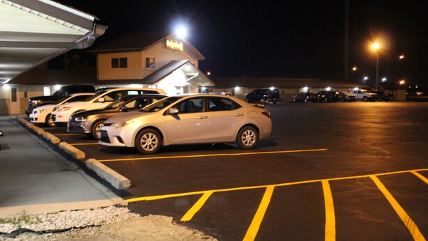 A parking lot with several cars parked, a building with a sign, and a well-lit street. - The Perrysburg Budget Inn (Perrysburg)
