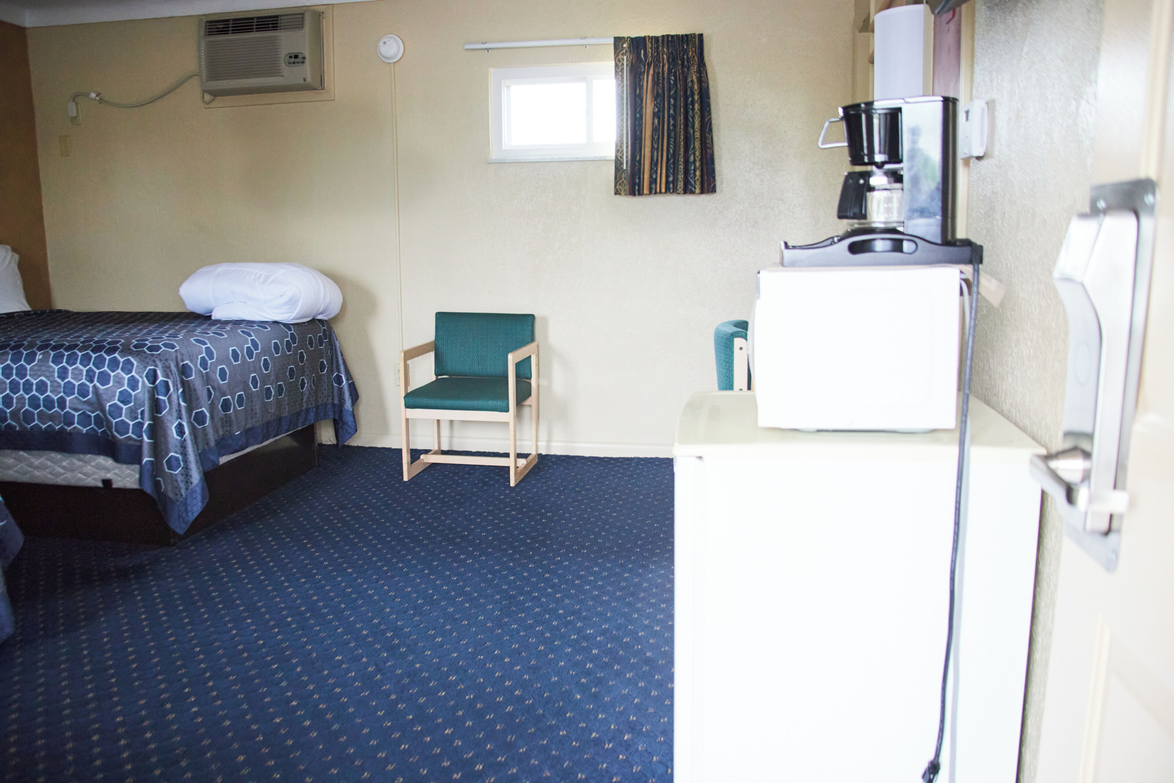 Une chambre d’hôtel avec un lit, une chaise, une machine à café et une fenêtre.