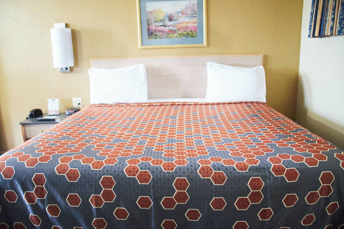 A hotel room with a large bed, a headboard, a nightstand, a lamp, and a painting on the wall.
