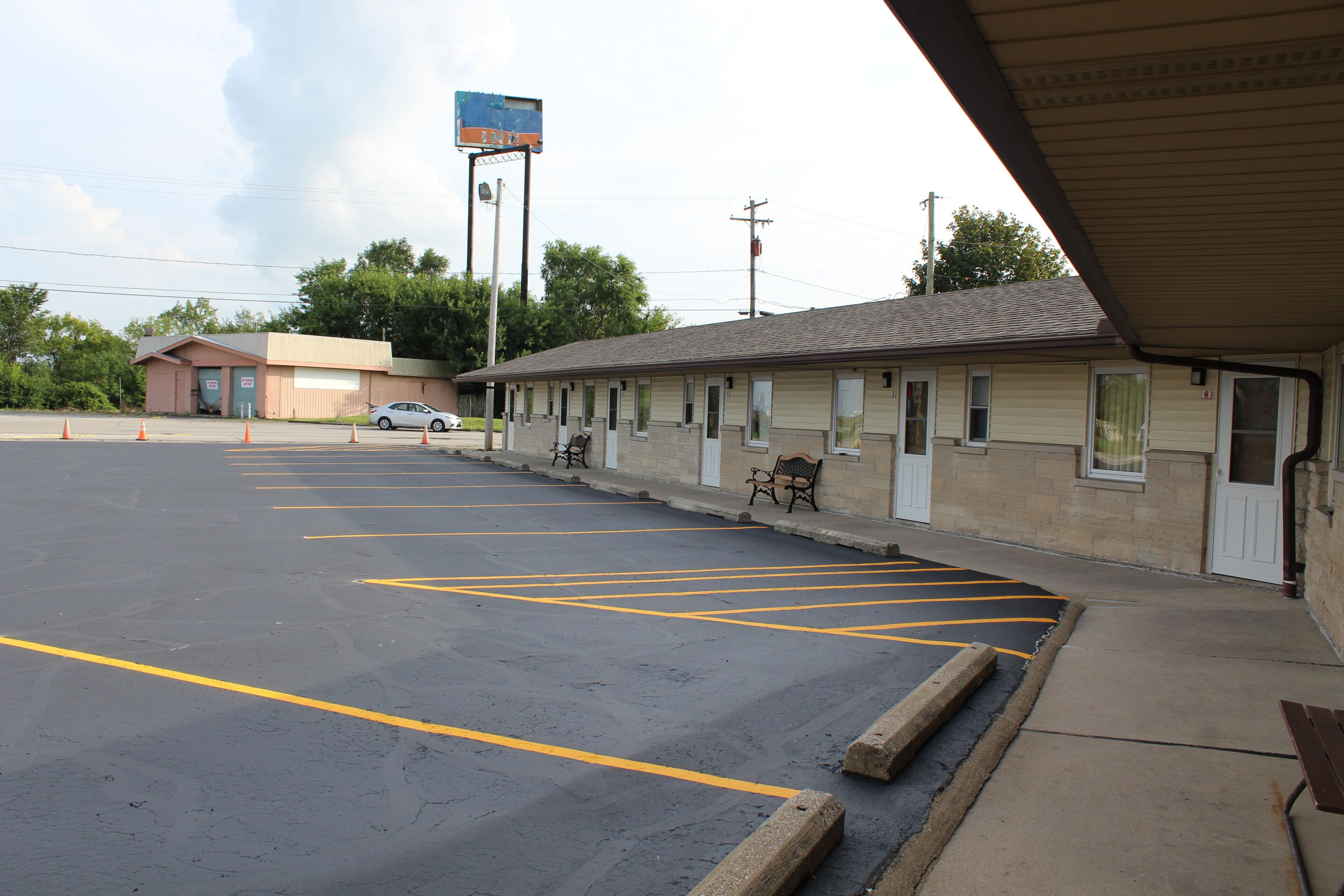 A motel with a parking lot, a row of rooms, and a signboard.