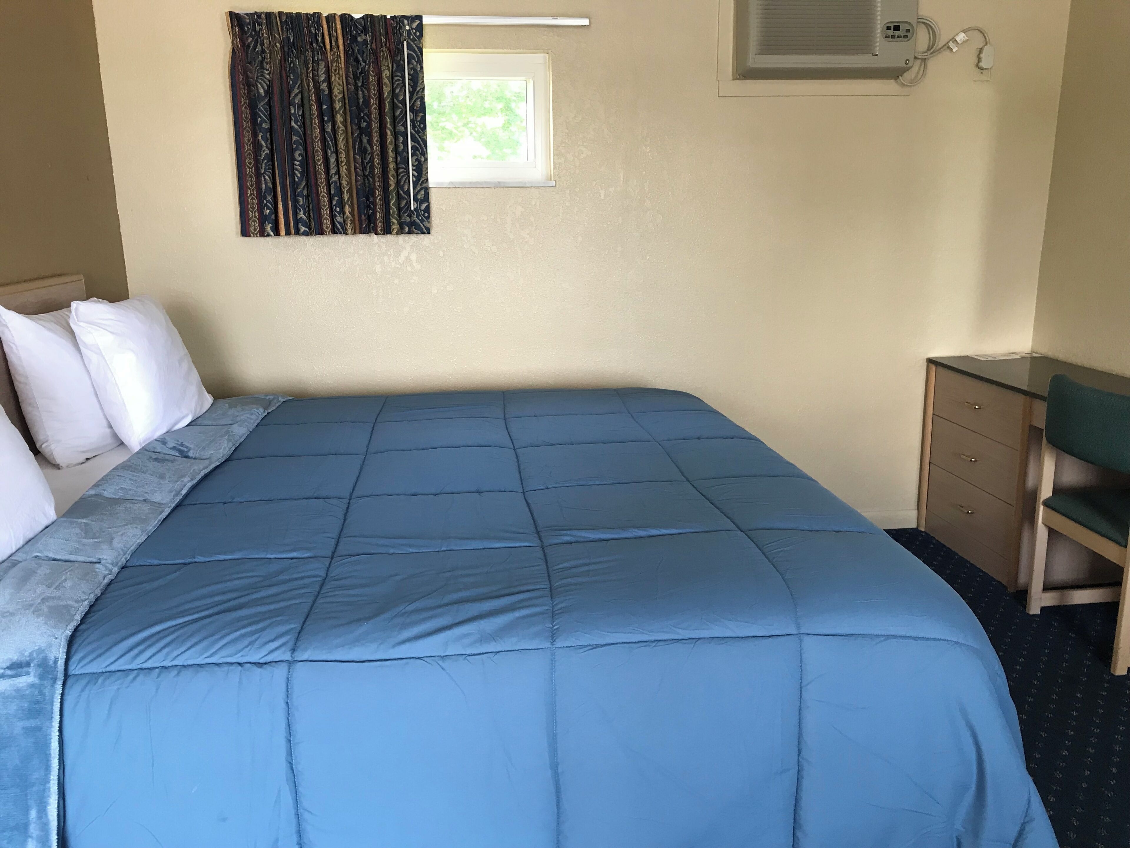 Una habitación con cama, escritorio, silla, ventana con cortinas y equipo de aire acondicionado.