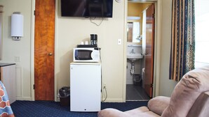A room with a television mounted on the wall, a microwave on a small white appliance, a door, and a view into a bathroom. - The Perrysburg Budget Inn (Perrysburg)