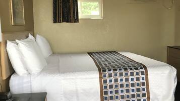 A hotel room with a bed, a desk with a telephone, a window with curtains, and an air conditioning unit.