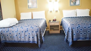 A hotel room with two beds, a nightstand, and a wall-mounted lamp. - The Perrysburg Budget Inn (Perrysburg)