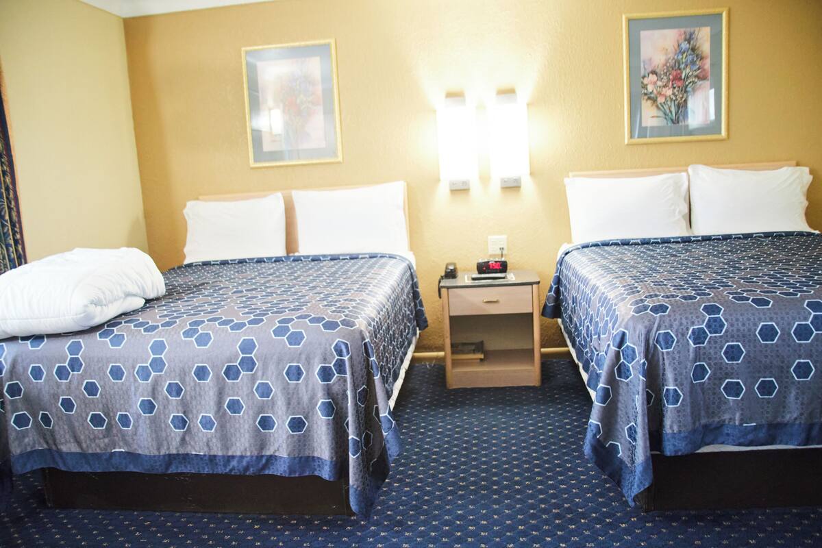 A hotel room with two beds, a nightstand, and a wall-mounted lamp.