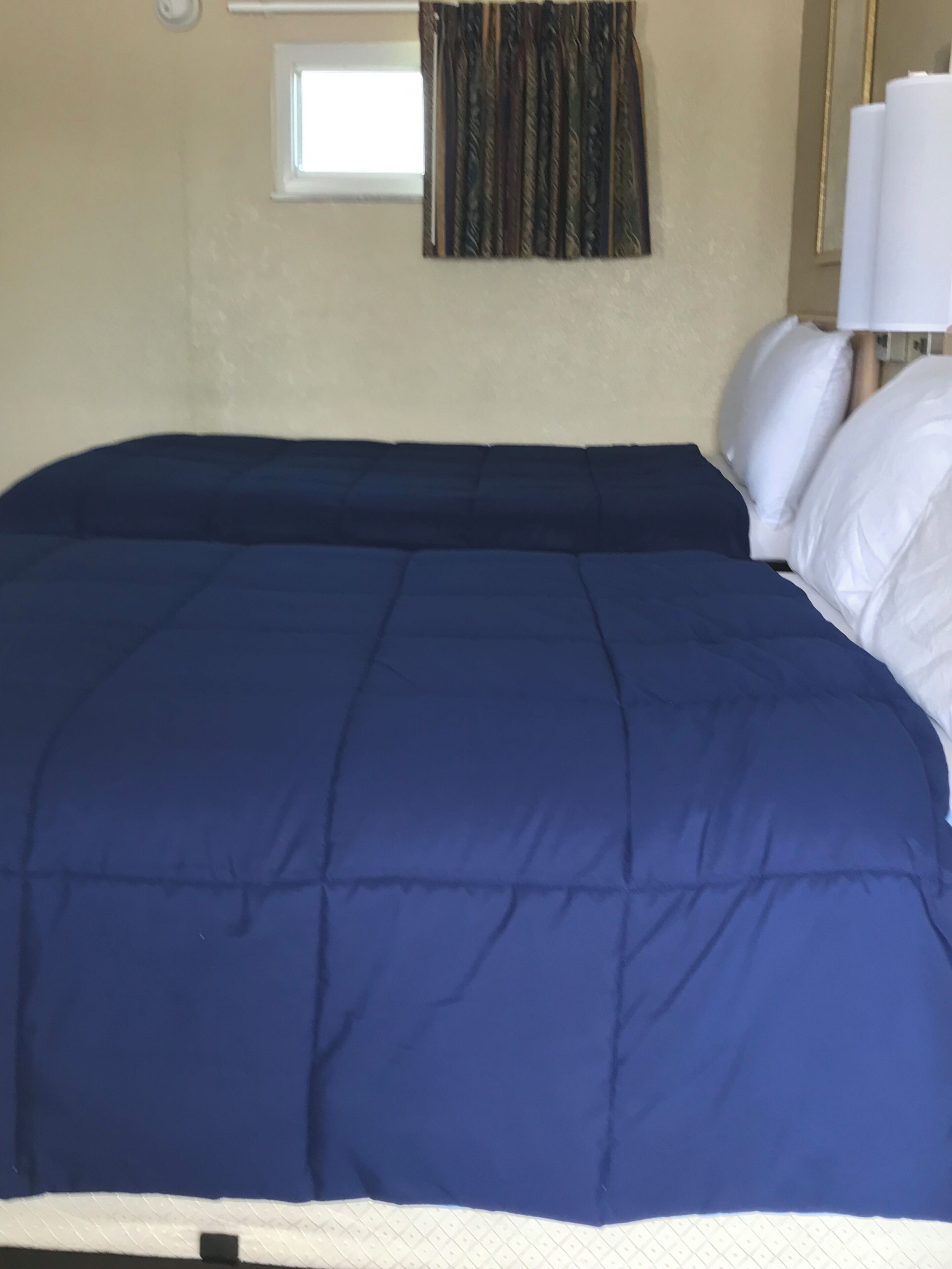 A bed with a dark blue bedspread and white pillows in a room with beige walls.