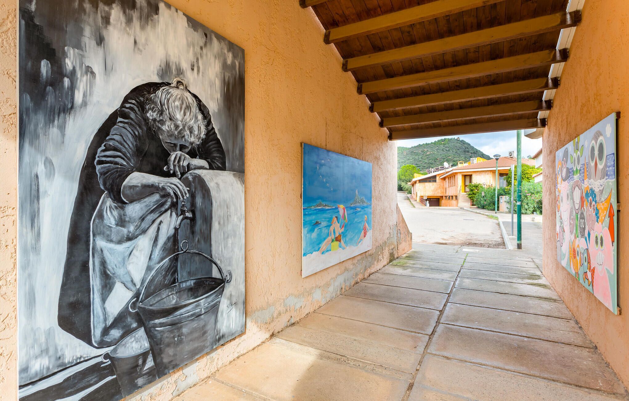 A corridor with a mural of a person with a bucket, a painting of a beach scene, and another mural of colorful owls.