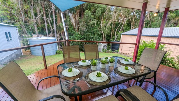 A covered outdoor patio with a table set for six, surrounded by chairs. - McLeods • Pet-Friendly Central Beach House in Agnes Water • Walk Everywhere (Agnes Water)