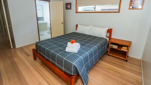 A bedroom with a bed, wooden floor, a nightstand, and a window with a view. - McLeods • Pet-Friendly Central Beach House in Agnes Water • Walk Everywhere (Agnes Water)