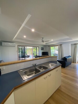 A modern kitchen with a built-in island, a dining area with a table and chairs, and a living room with a sofa. - McLeods - Relaxed Pet-Friendly Stay by the Beach (Agnes Water)