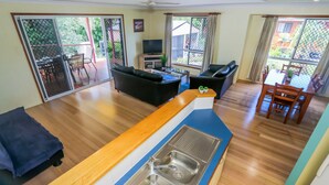 A spacious living area with a kitchen island, sliding glass doors to a patio, and a dining table with chairs. - McLeods • Pet-Friendly Central Beach House in Agnes Water • Walk Everywhere (Agnes Water)