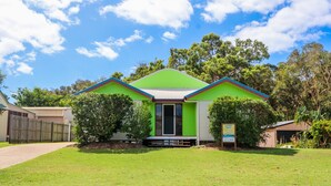 A small, single-story building with a green roof and a sign indicating it is a holiday home. - McLeods • Pet-Friendly Central Beach House in Agnes Water • Walk Everywhere (Agnes Water)
