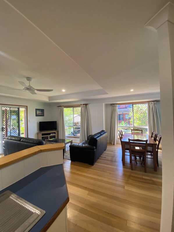 A spacious living area with a sofa, a dining table with chairs, a television, and a ceiling fan.