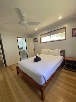 A bedroom with a bed, a ceiling fan, a window, and a wooden floor.