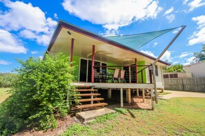 A house with a covered porch, a staircase leading to the entrance, and a large shade sail.