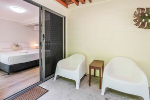 A room with a bed, a small table, two white chairs, and a sliding glass door leading to another room. - Merindah • Pet-Friendly Central 4BDR in Agnes Water • Walk Everywhere (Agnes Water)