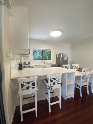 A modern kitchen with white cabinetry, a central island, and a dining area with white chairs.