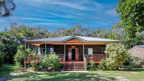 A wooden house with a porch, surrounded by lush greenery.