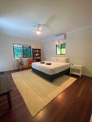 A bedroom with a bed, a bedside table, a chair, a bookshelf, and a ceiling fan.