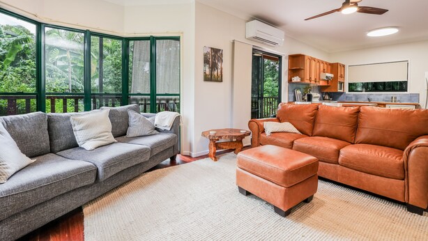A living room with a grey sofa, an orange leather sofa, a wooden coffee table, and a large window with a view of greenery.