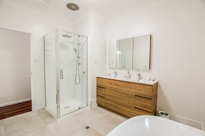 Un baño moderno con ducha envuelta en vidrio, tocador de madera y un espejo grande.