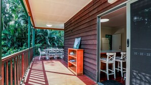 A wooden deck with a railing, a small table and chairs, and a bookshelf.