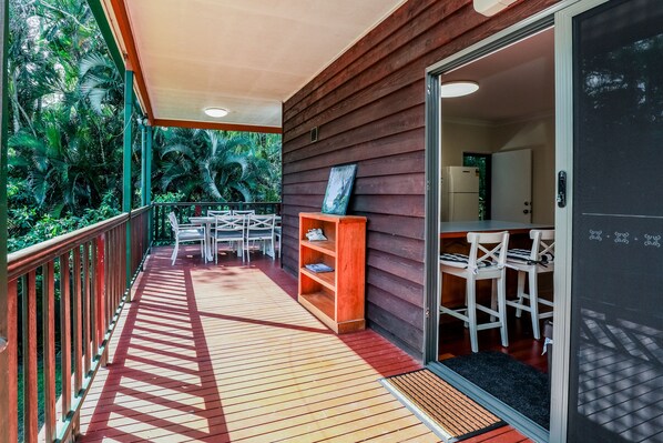 A wooden deck with a railing, a small table and chairs, and a bookshelf.