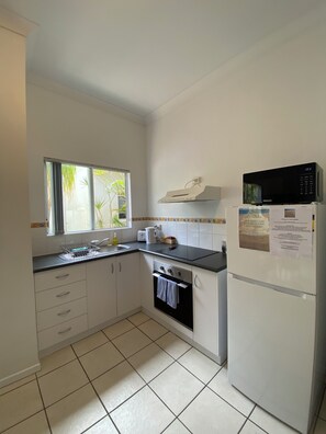 A compact kitchen with white cabinets, a black countertop, a built-in oven, a microwave, and a refrigerator.