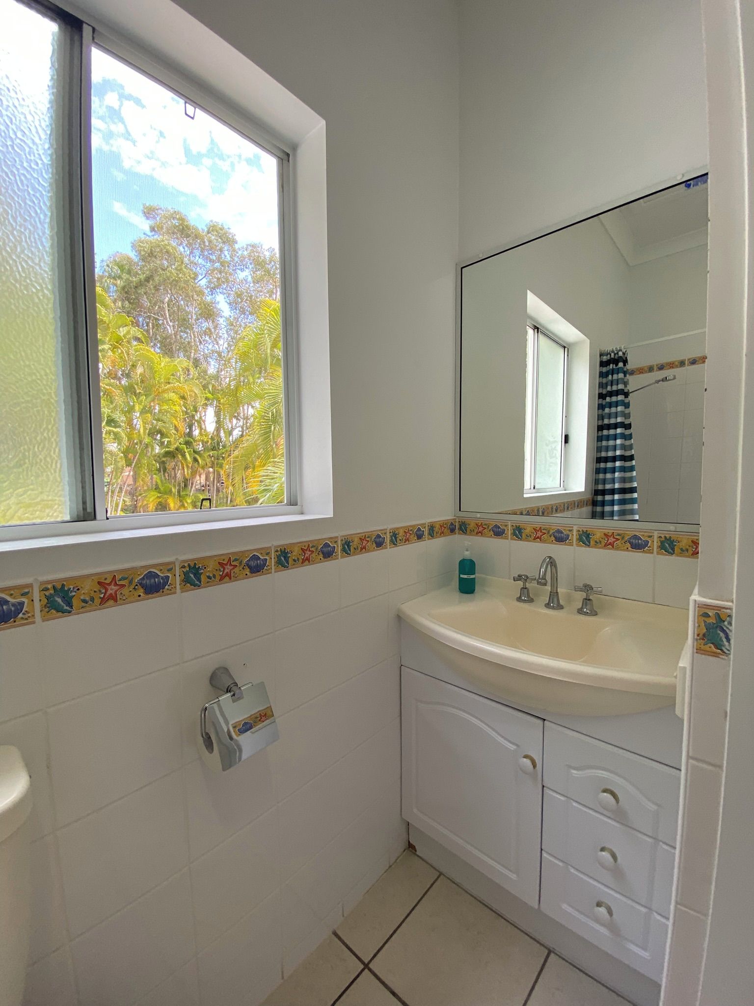 A bathroom with a window, a sink, a mirror, and a toilet.