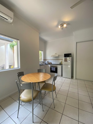 A compact kitchen with a dining area, featuring a round table, chairs, a refrigerator, a microwave, and a window with a view of greenery.