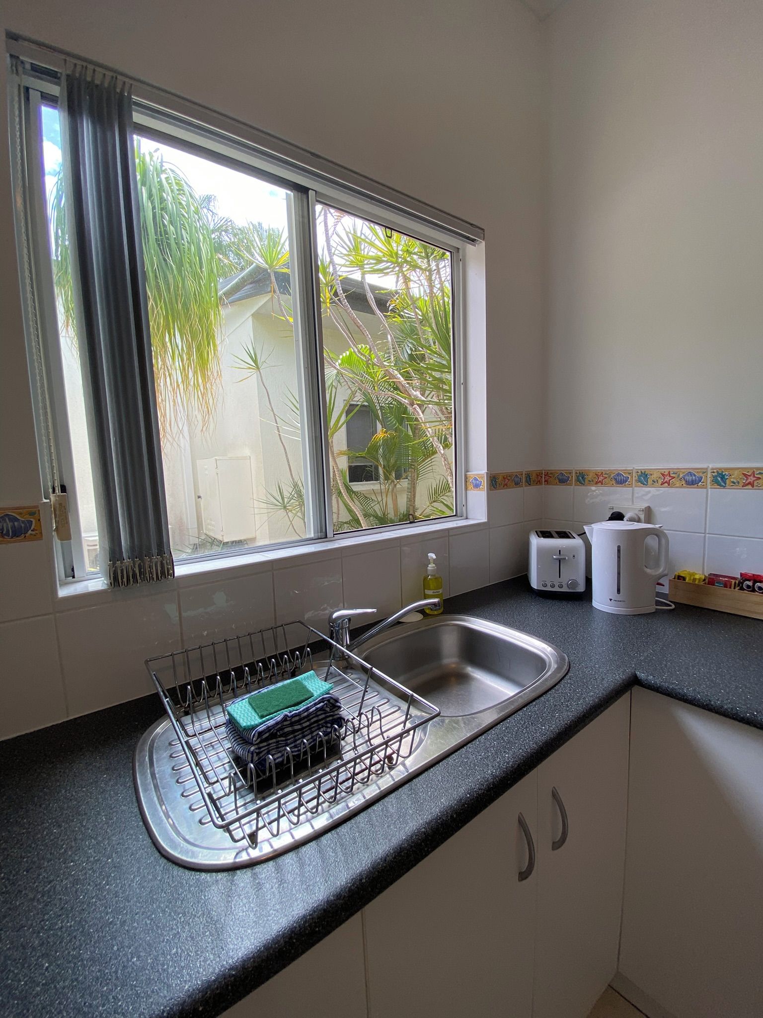 A kitchen with a window, a sink, a dish rack, a toaster, and a kettle.