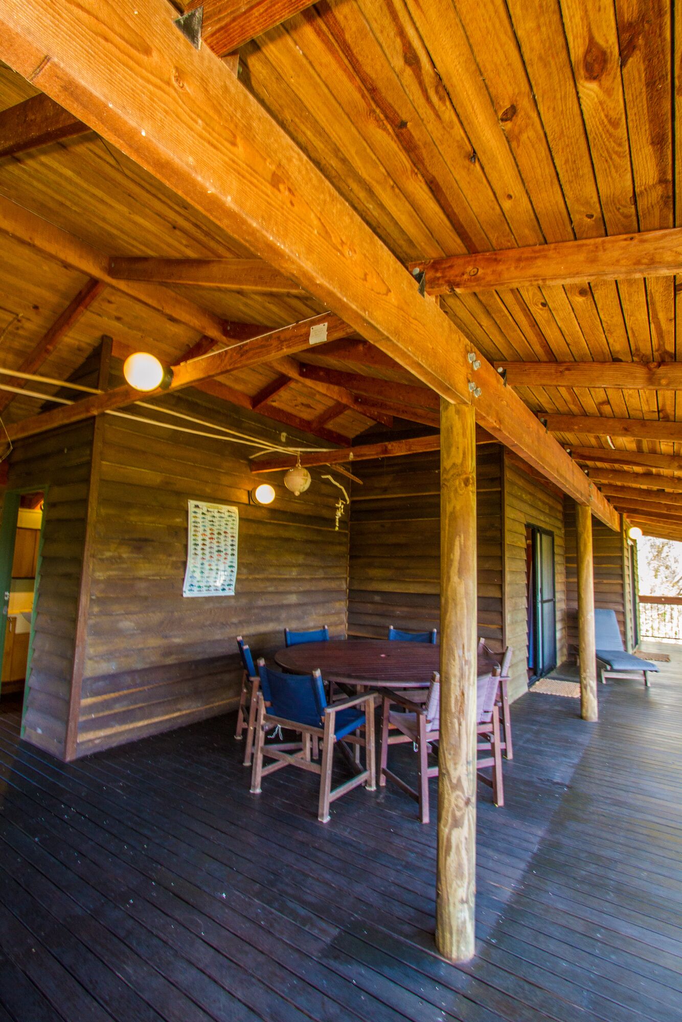 Eine überdachte Holzterrasse mit Tisch und Stühlen, Holzwänden und einer Decke mit freiliegenden Balken.