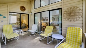 A covered outdoor seating area with chairs and a table, large windows, and a decorative wall piece.