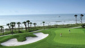 A golf course with sand bunkers, a person playing golf, and a view of the ocean.